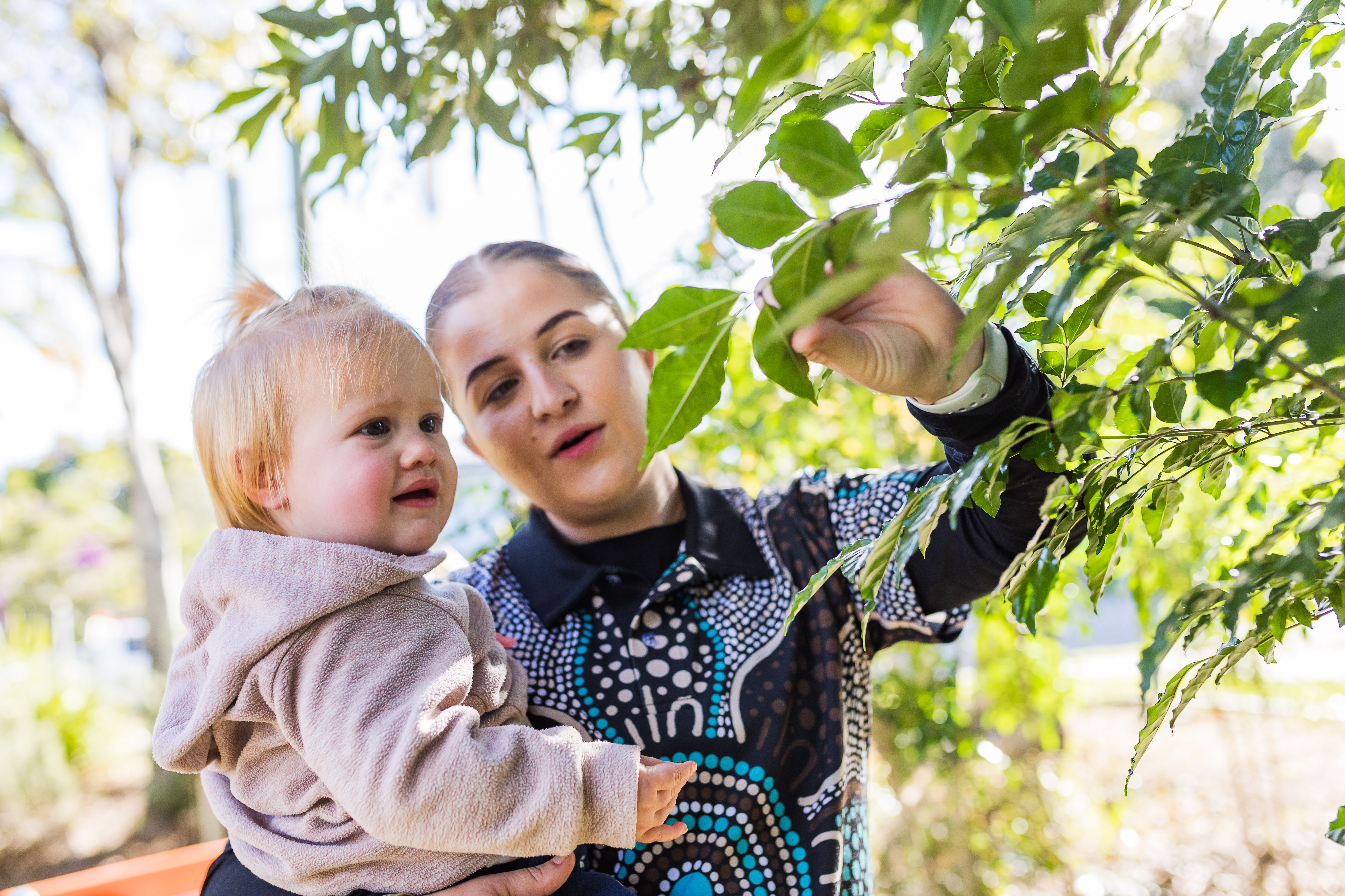Educator and baby together outside lookng at leaves
