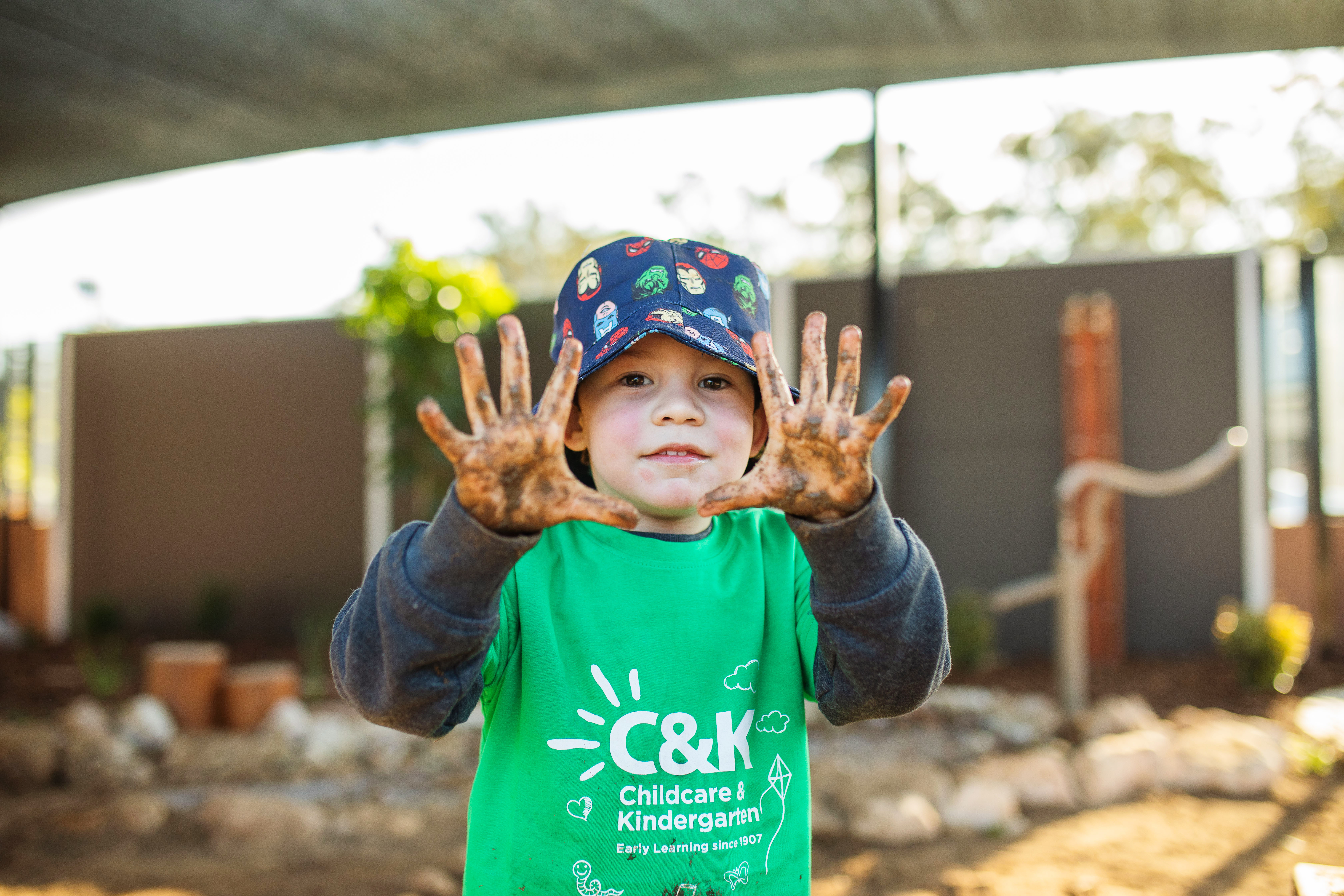 Child looking at camera holding up hands covered in mud