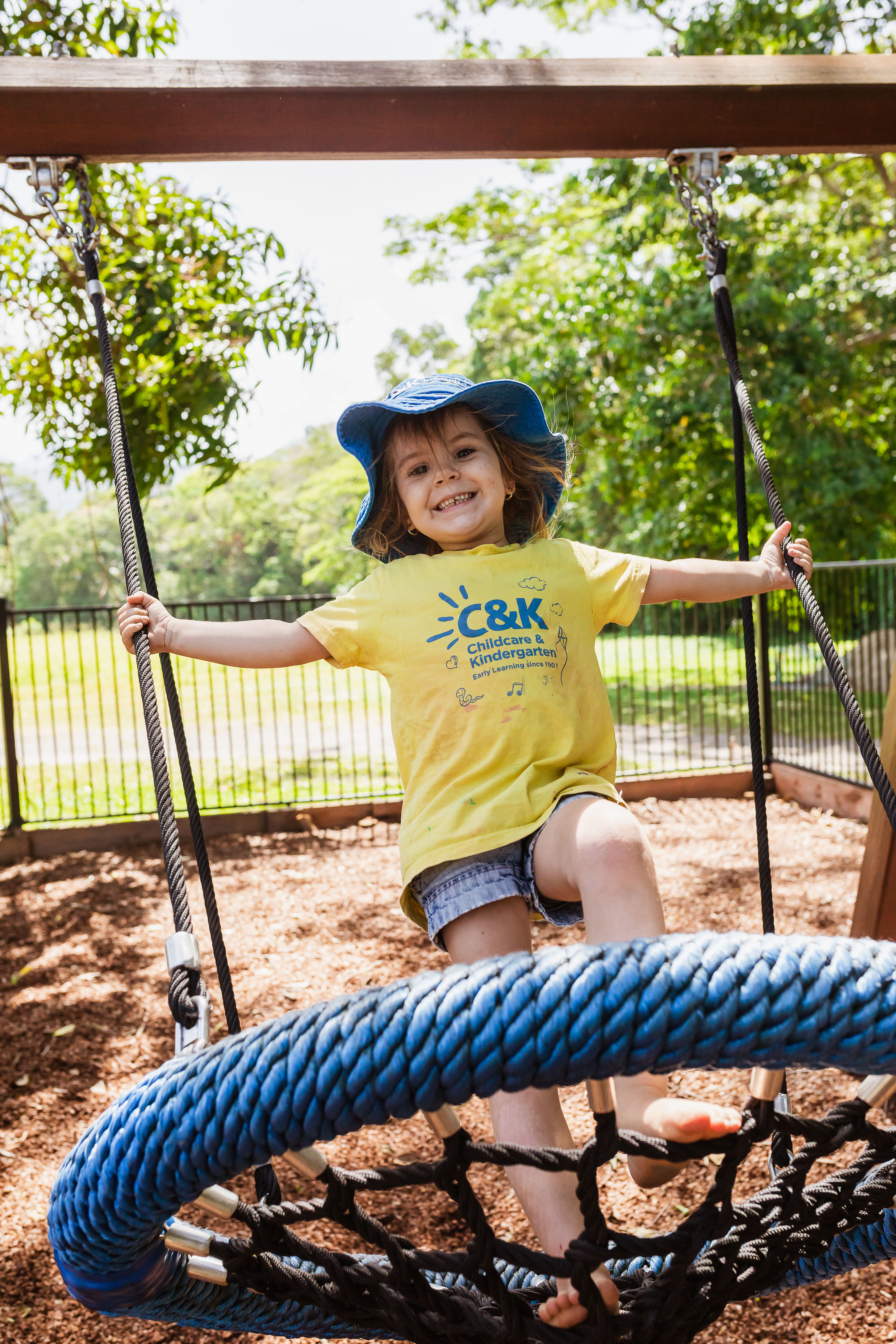 C&K kindy child smiling standing on a swing mid air