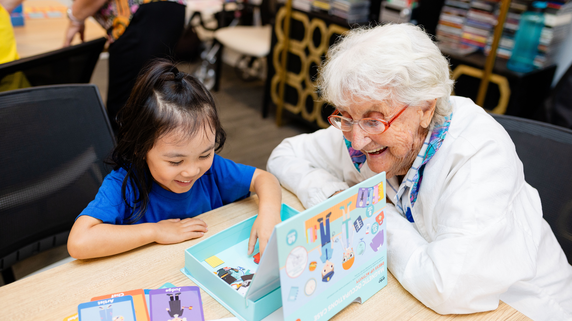 Elderly woman and kindergarten child at table smiling doing an activity