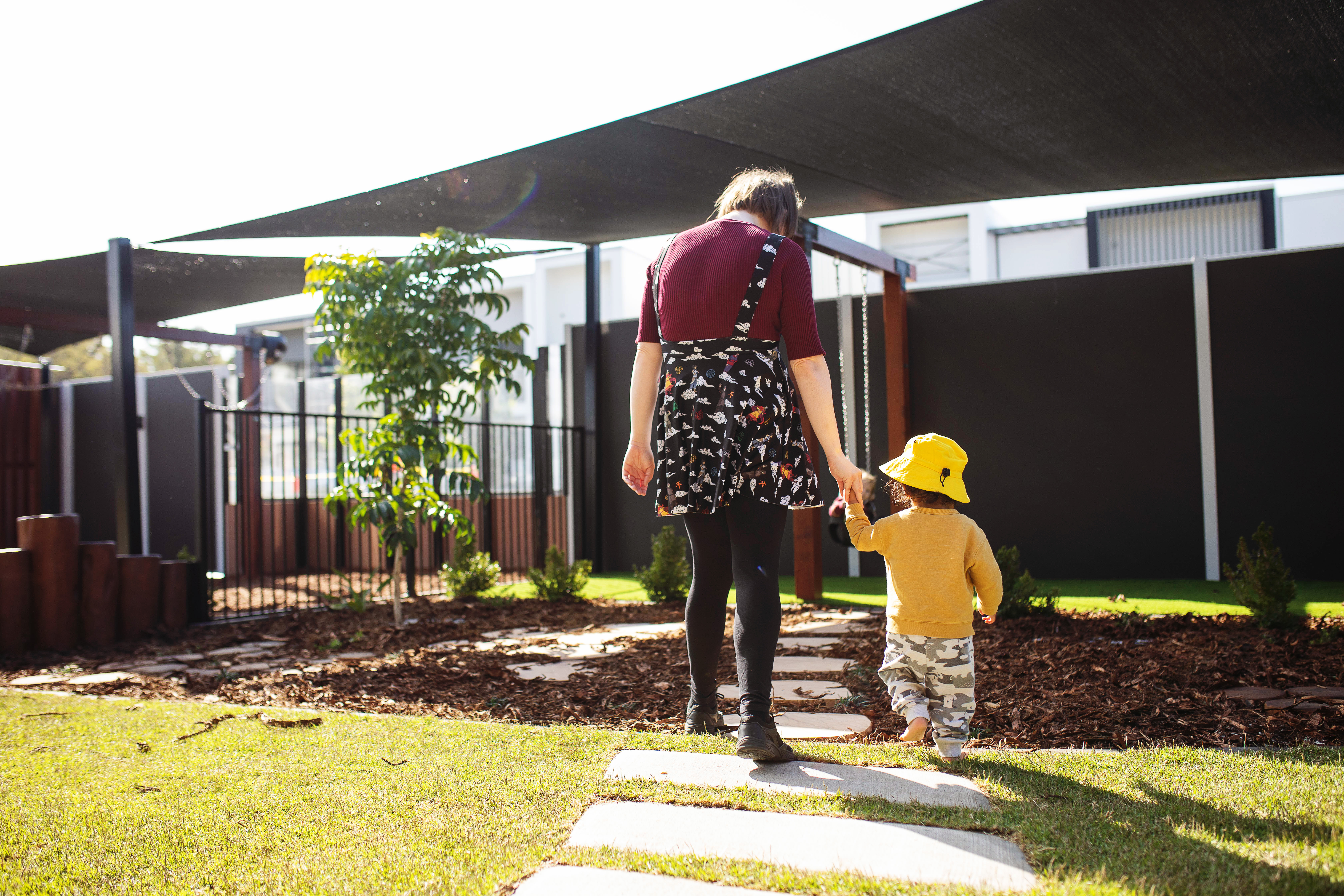 An educator and child holding hands walking together outside