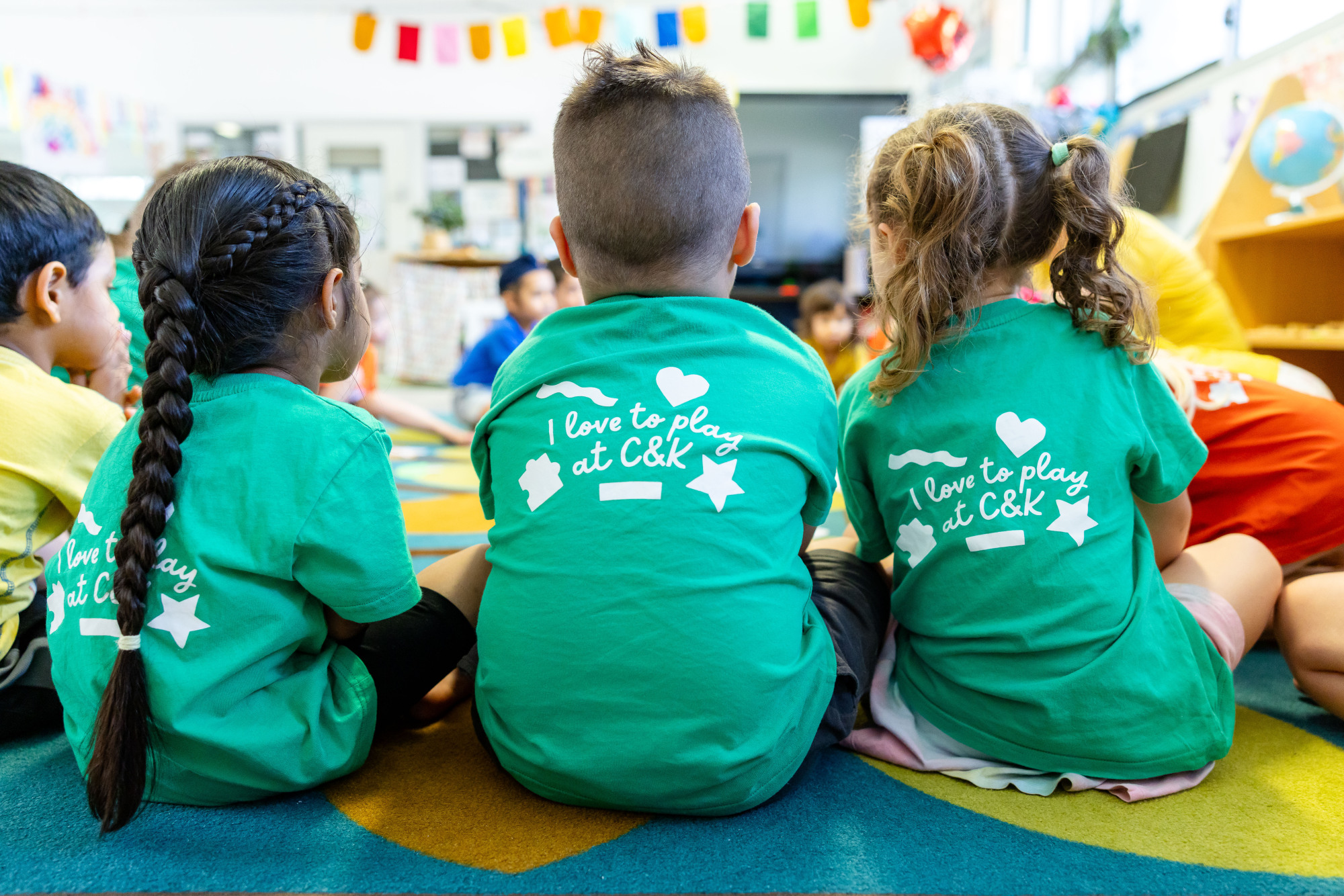 Three kindy children sitting next to each other in green C&K shirts