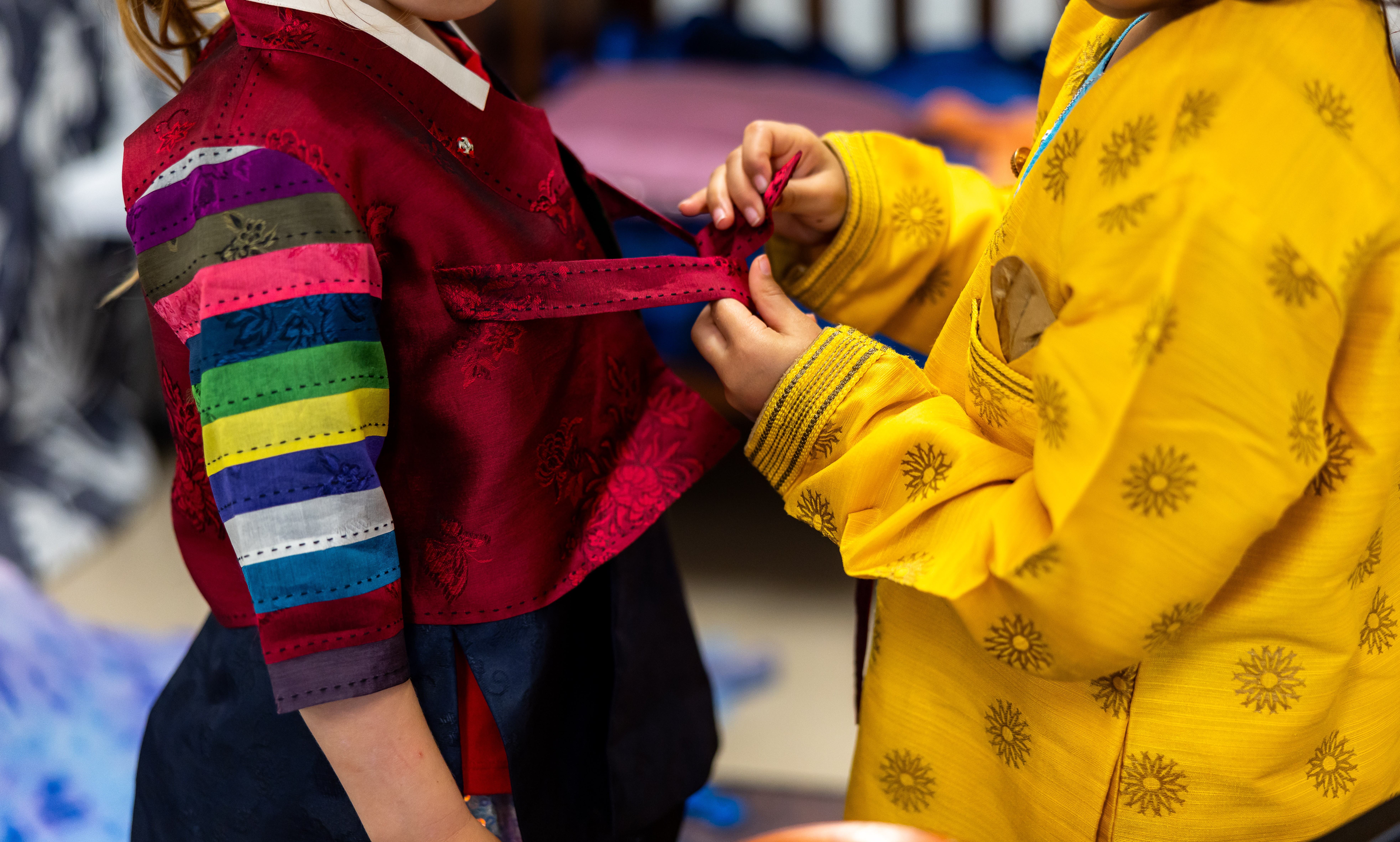Child helping to do up buttons on colourful cultural outfits