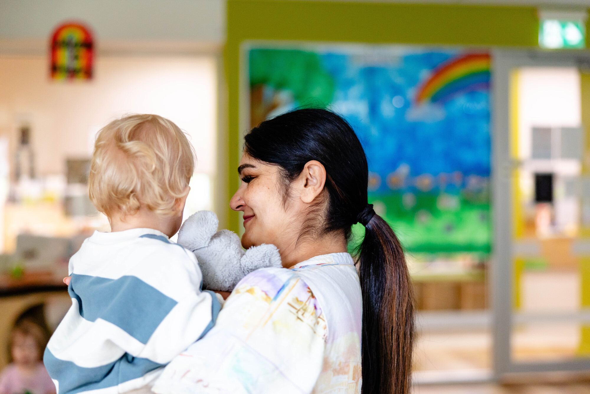 Educator holding a toddler, smiling.