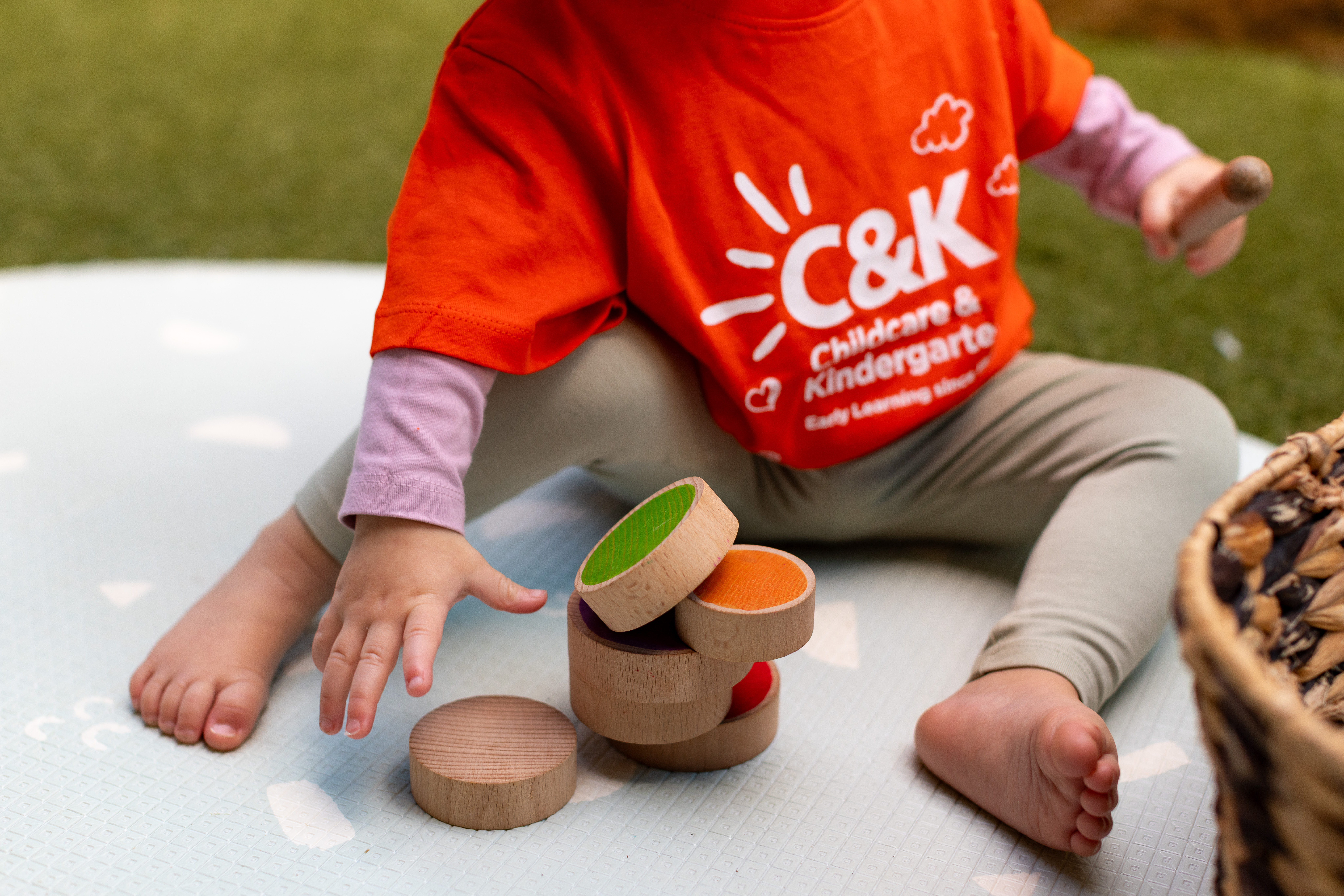 Little toddler in an orange C&K shirt stacking colouful wooden blocks