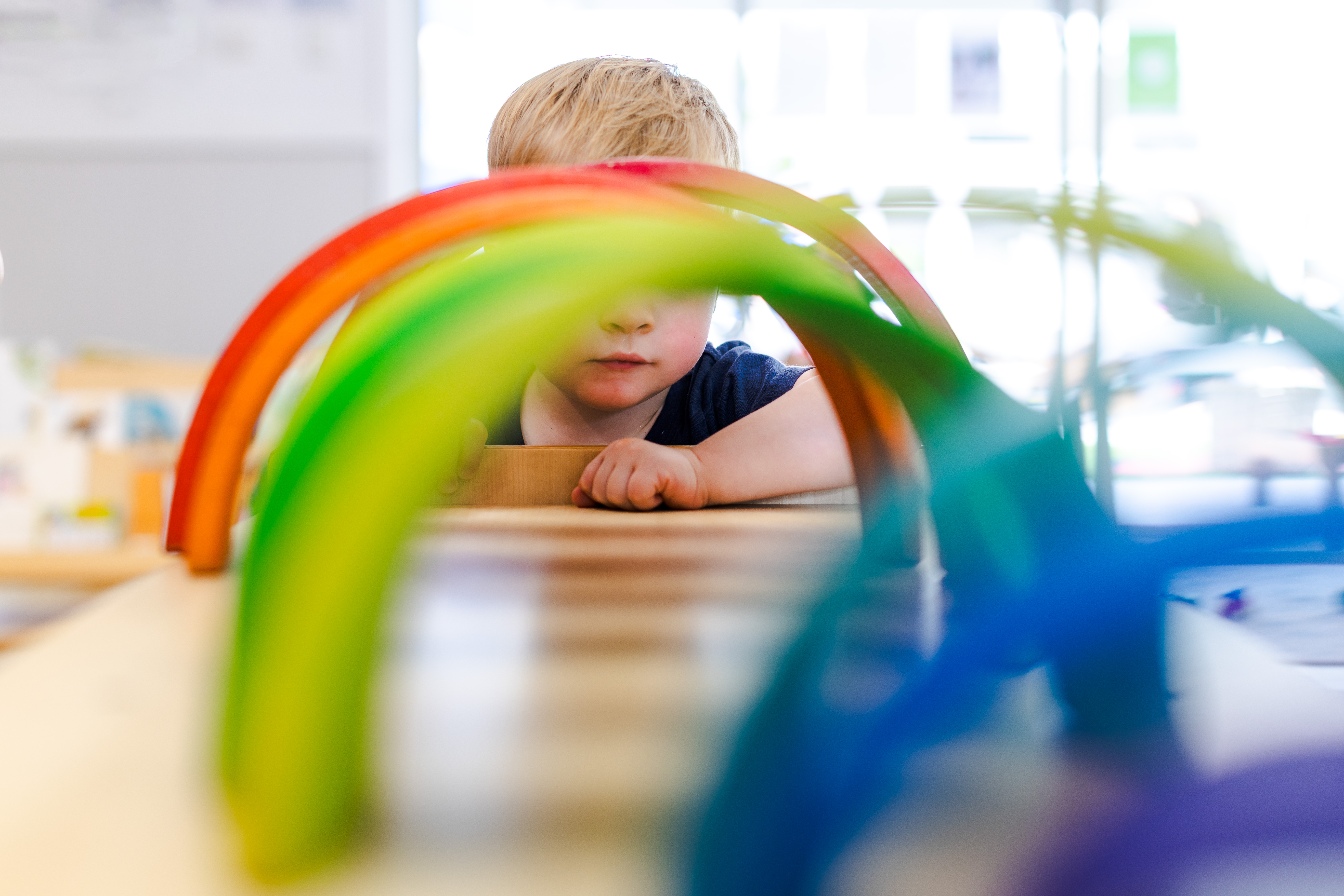 Child looking through a colourful wooden rainbow inside