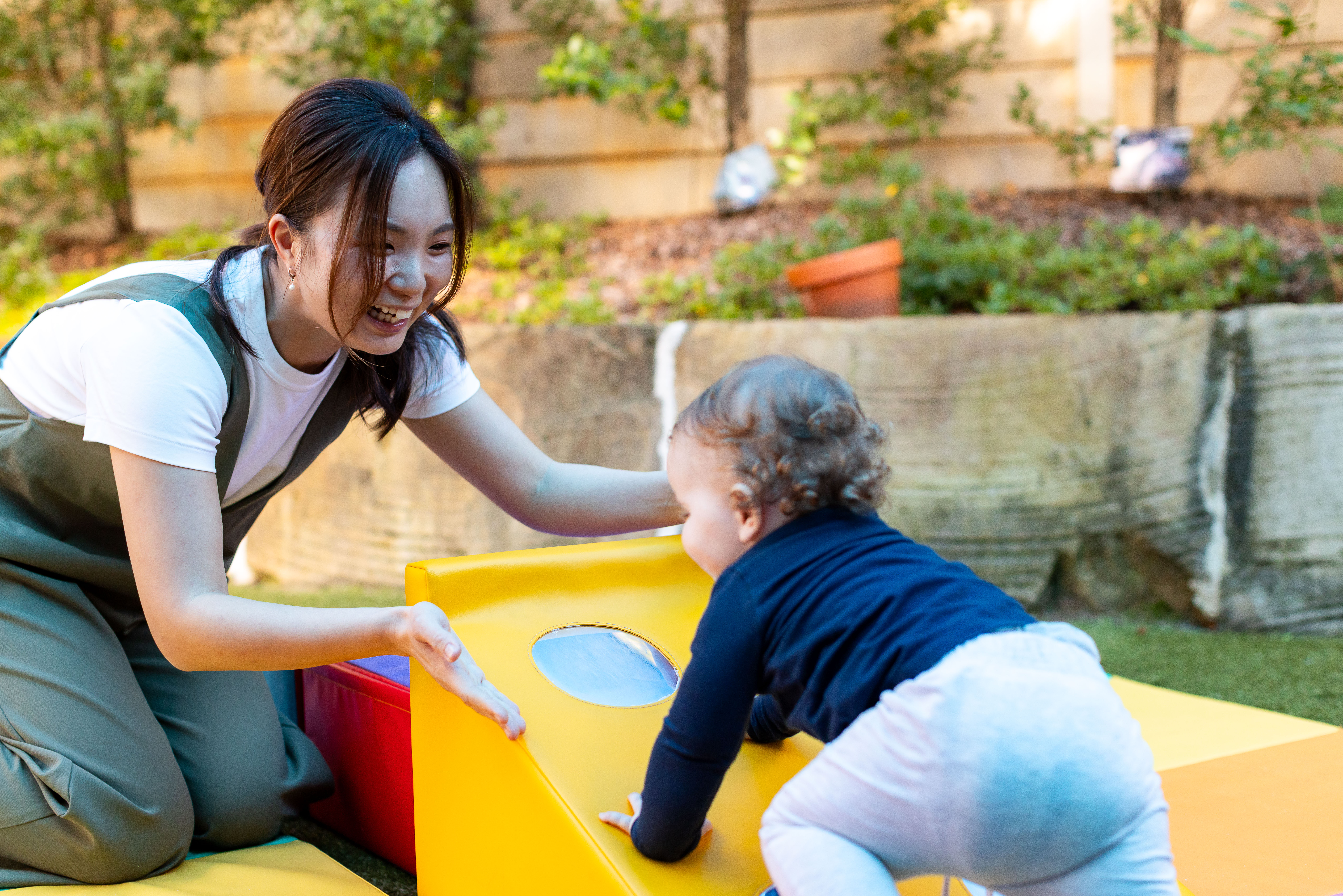 Baby crawling up colourful soft play to smiling educator