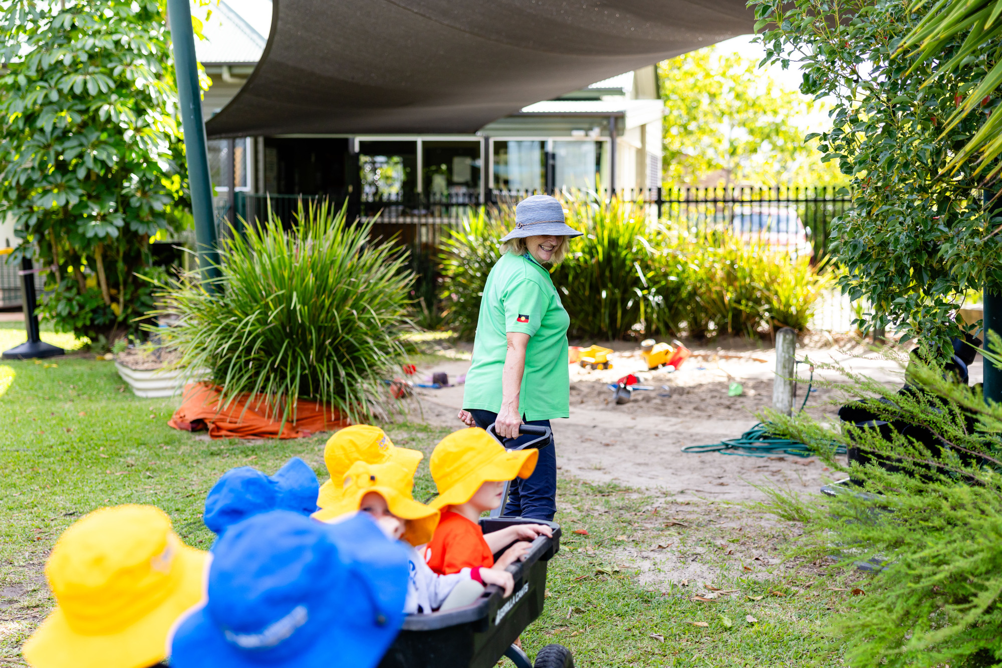C&K Caboolture - children sitting in a cart being pulled by a smiling educator