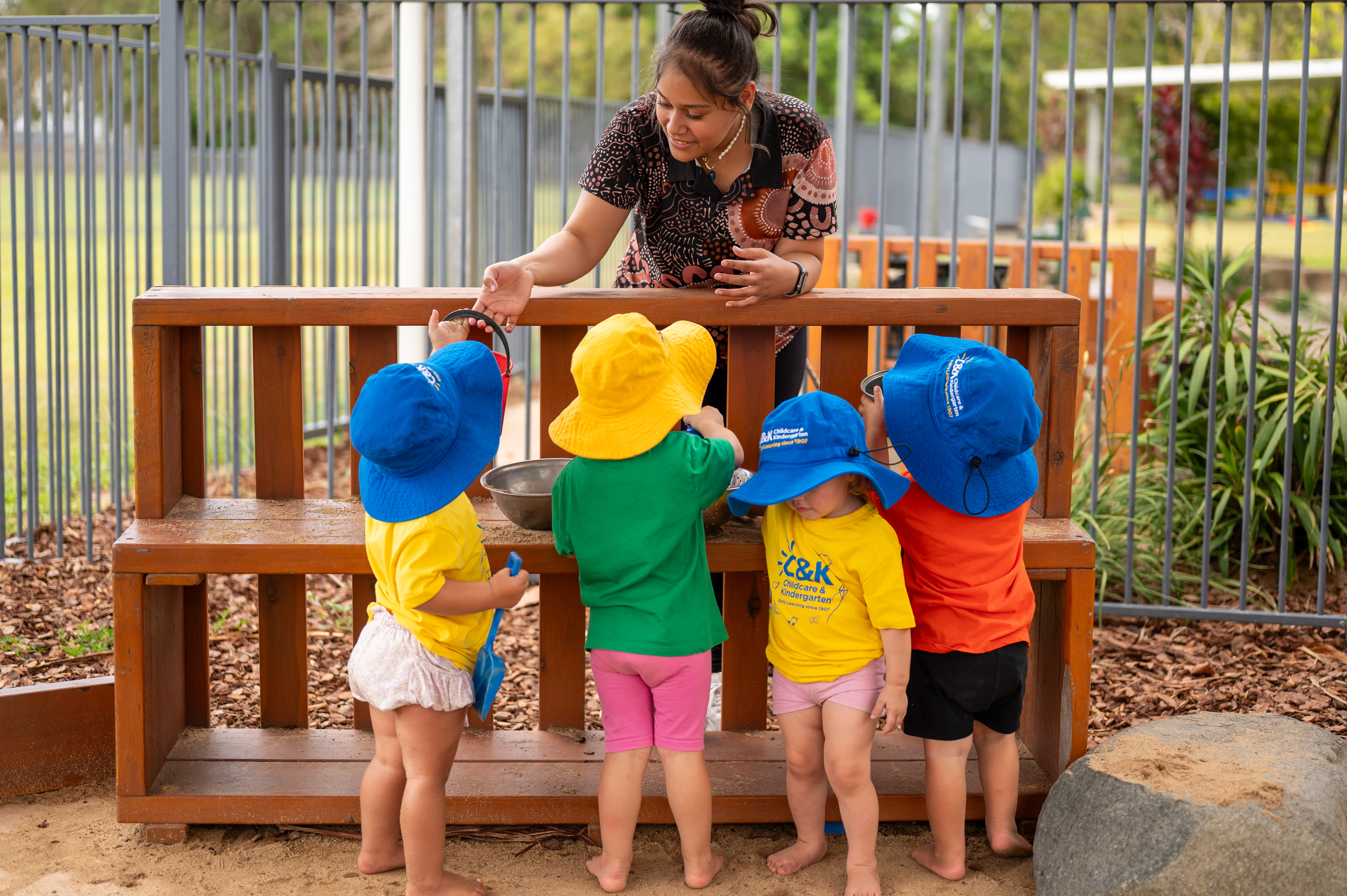 C&K Mackay CFC - educator and toddlers playing in the mud kitchen