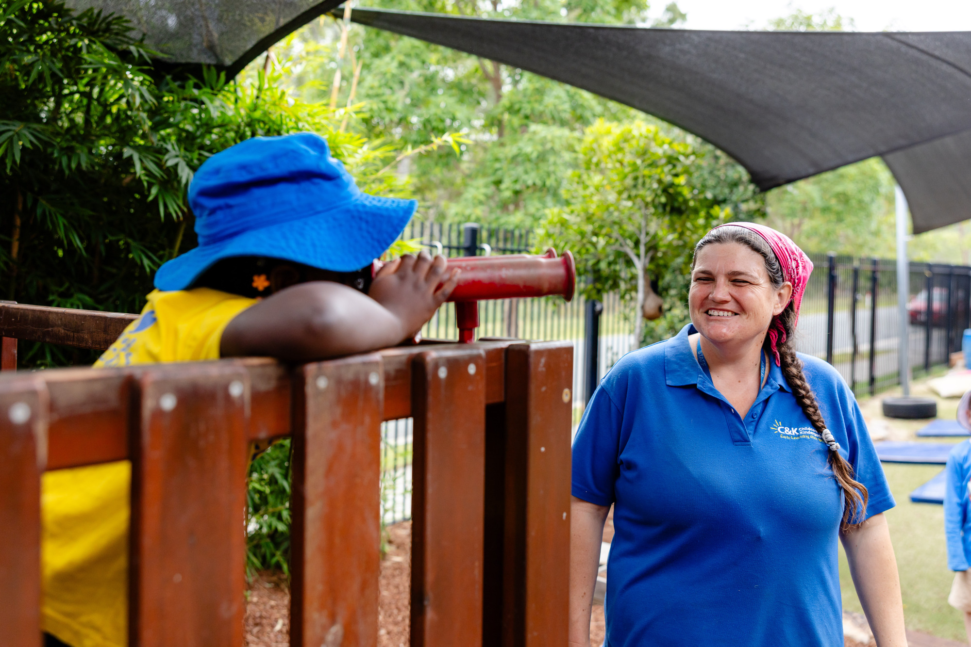 C&K Ripley - child on the fort playground looking through binoculars, with an educator standing nearby smiling