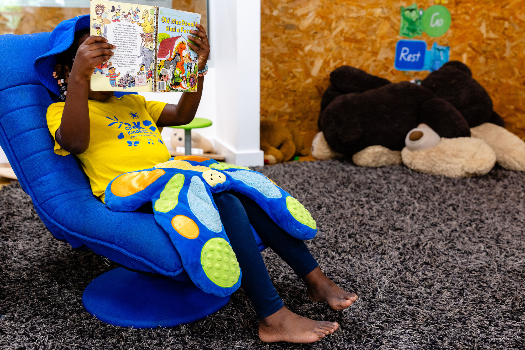 C&K Ripley - child indoors reading a book, with a weighted toy in her lap