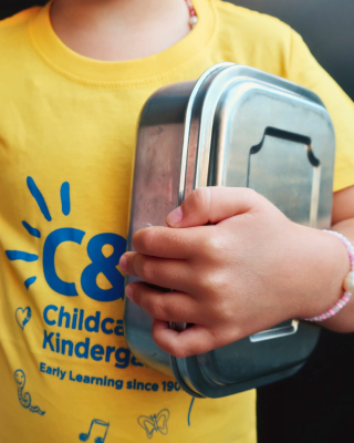 Photo of a child holding a lunchbox, wearing a C&K shirt.
