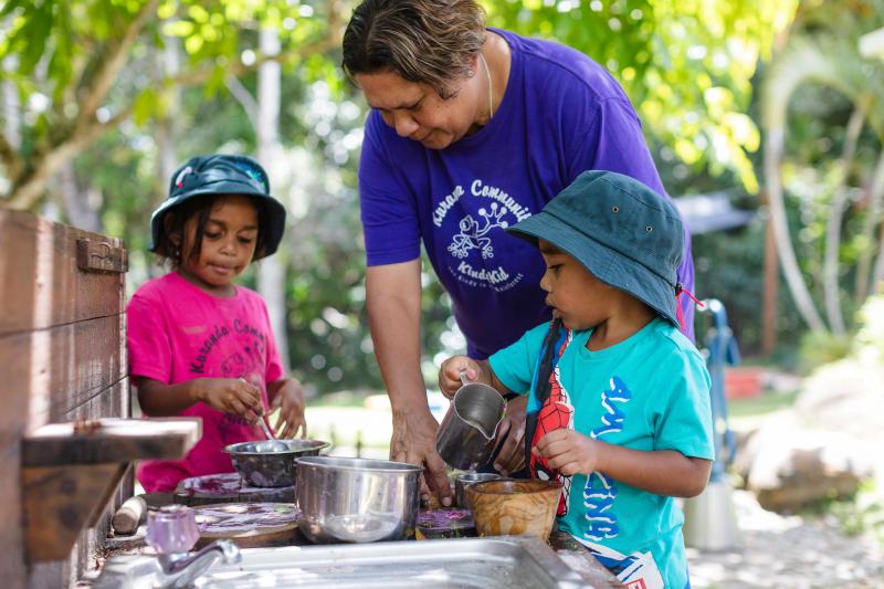 Educator and two children playing outside under the trees