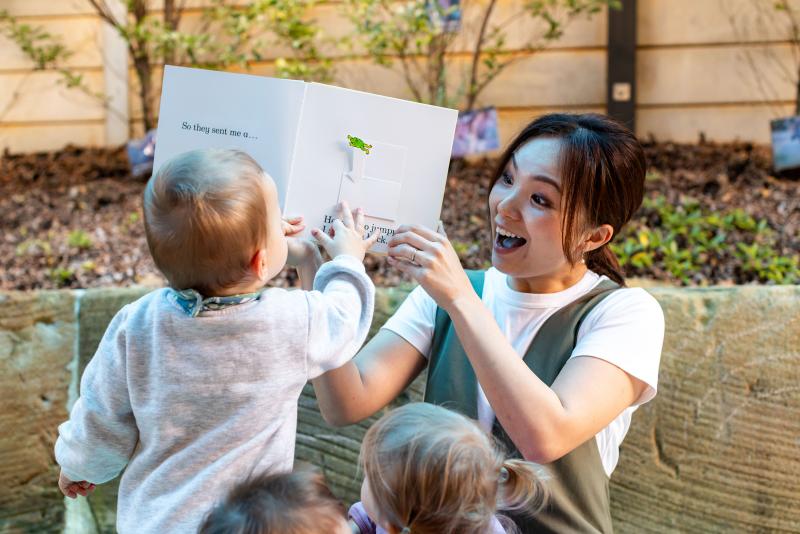 Smiling educator reading a story and engaging with toddlers