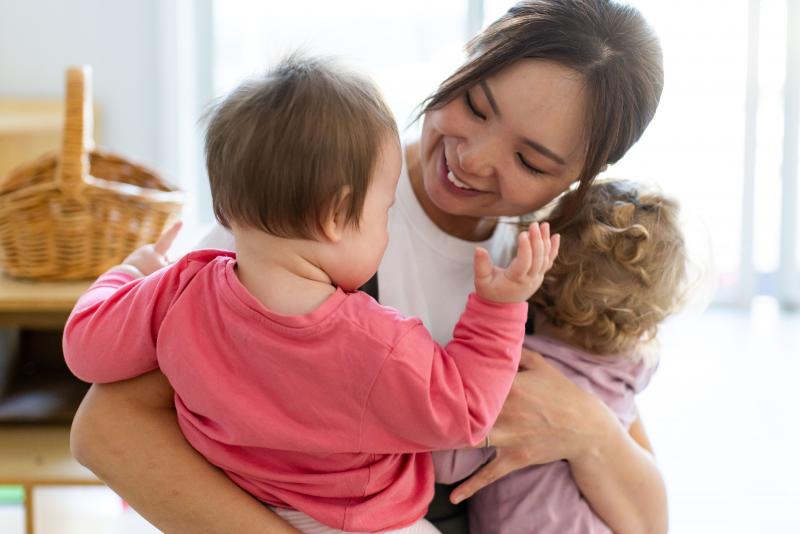 Smiling educator cuddling two babies