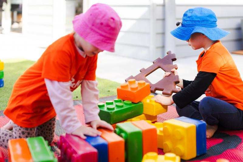 Two kindy children playing outside with colourful blocks