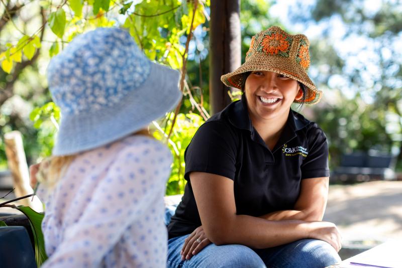 Educator smiling and sitting outside with kindy child