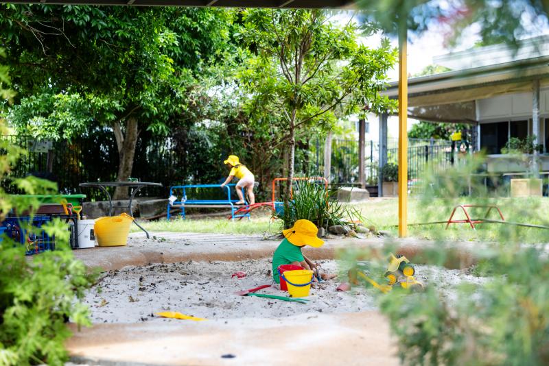 Children playing in the sandpit outside surrounded by leafy trees