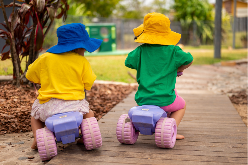Two toddlers riding off together on trikes