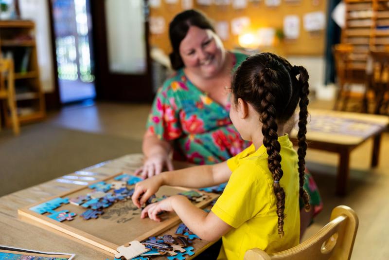 Teachers smiling at kindy child while doing a puzzle together