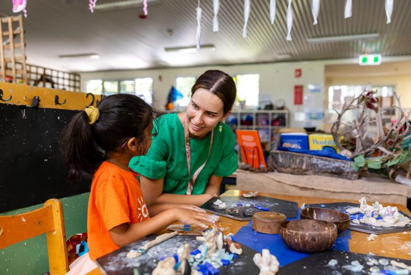 Educator sitting with child, smiling and engaging in clay