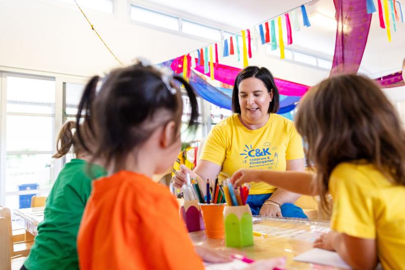 Smiling C&K educator sitting with kindy children