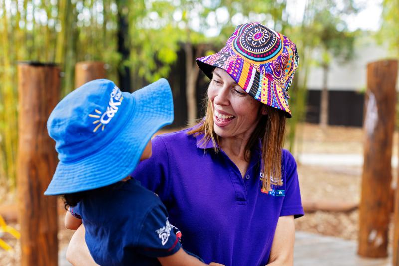 Educator smiling with a child outside wearing hats