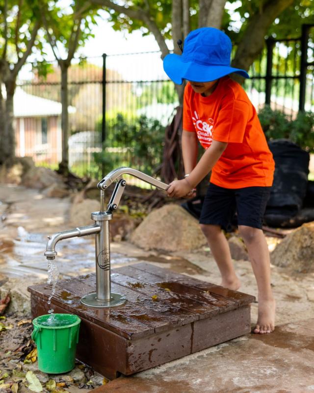 child pumping water from a water pump into a bucket