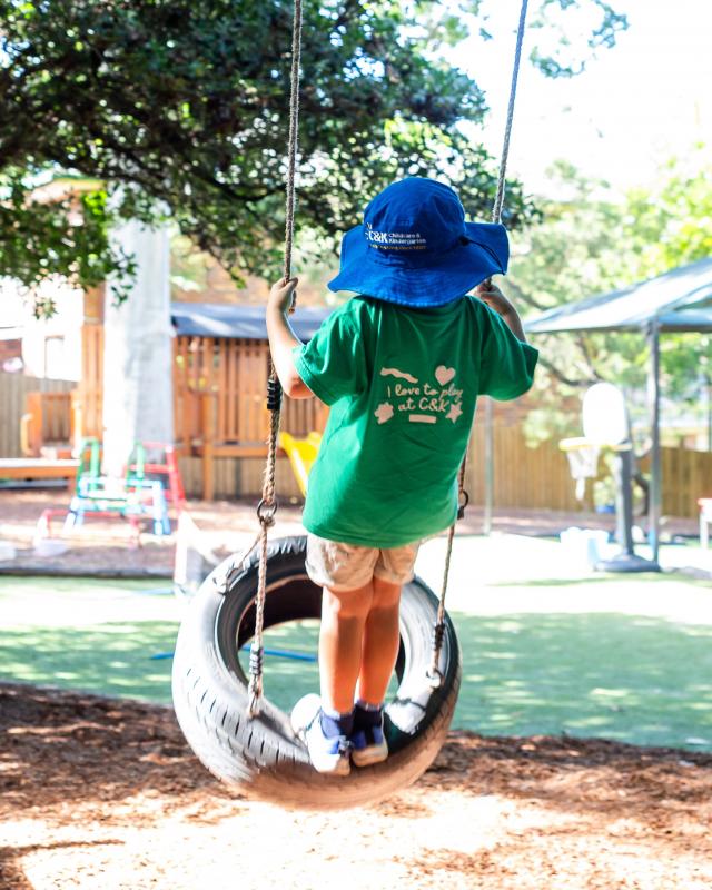 C&K kindy child standing on a swing mid air