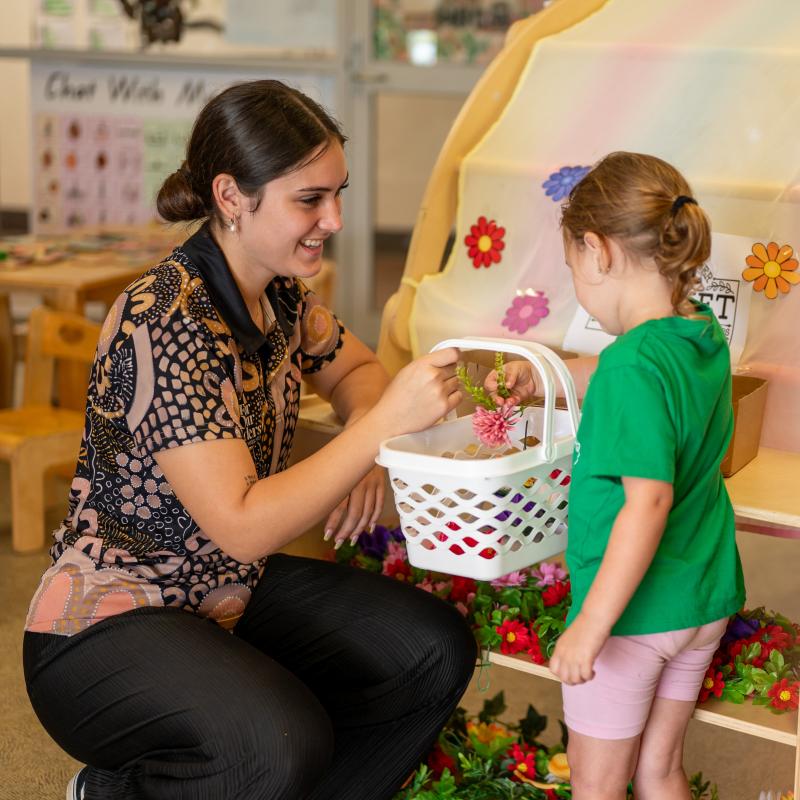 Home page slider 3 - educator smiling at child while they role play in a flower shop