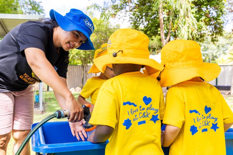 Kindy educator and children playing with water outside