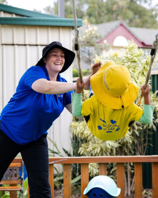 An educator pushing a child on a swing, smiling.