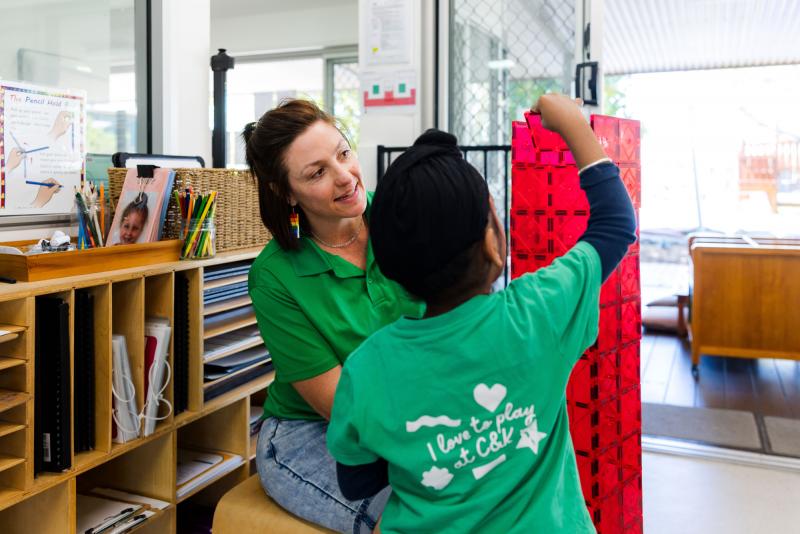 Educator supporting a child to build a tower out of magnetic tiles.