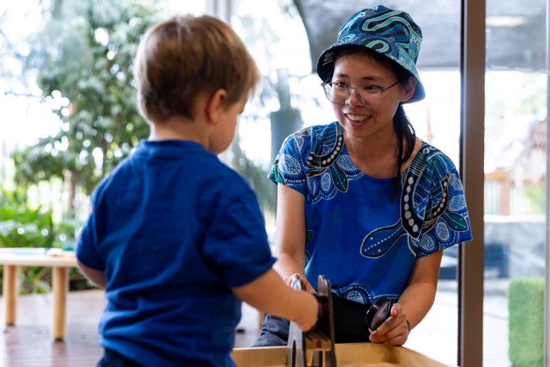 Educator crouching down to a toddler's height, smiling at them.