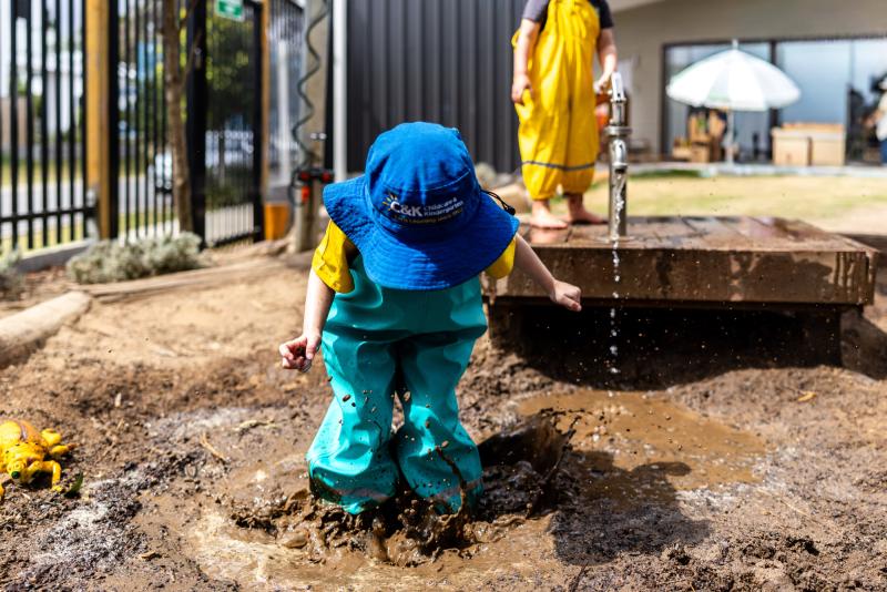Kindy child jumping barefoot in muddy puddle